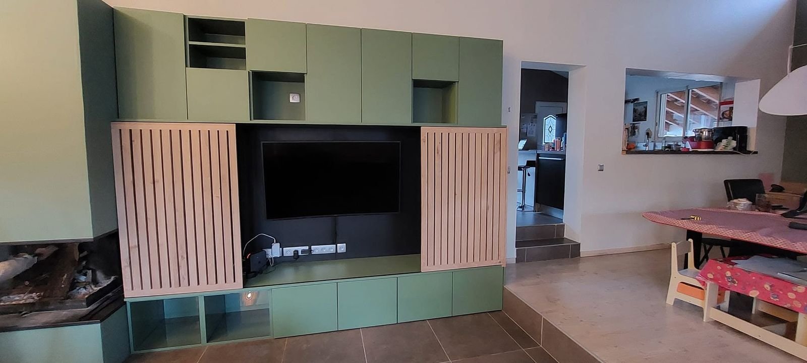 Mur complet de salon sur mesure : meuble TV vert, niches et claustras coulissants en chêne